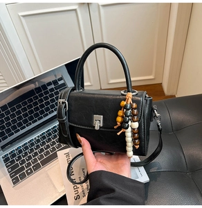 Detailed view of black square handbag with silver metal buckle and wooden bead charm accessory