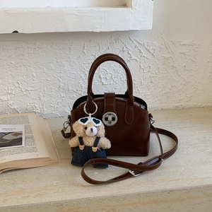 Detail of vintage brown leather handbag with round metal lock and cute teddy bear charm