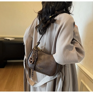 Detail view of a dark brown leather hobo bag with gold logo and woven strap ornament