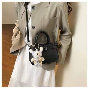 Detail of black pebbled leather handbag featuring a plush bunny charm on a grey suit model