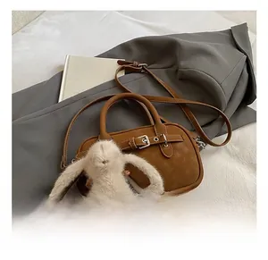 Close-up of vintage brown leather handbag with metal buckle and fluffy rabbit pendant