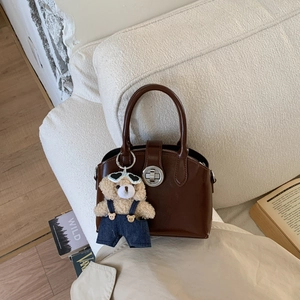 French vintage brown handbag with glossy finish and a cute teddy bear charm on white sofa