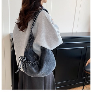 Detail of dark grey washed denim crescent bag with decorative side drawstring bow knots