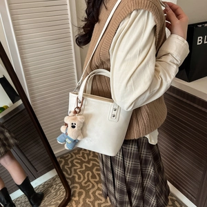Close-up of a white bucket bag with a cute teddy bear charm and adjustable shoulder strap