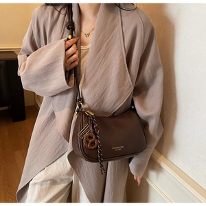 Detail of dark brown leather half-moon bag with decorative charms and golden logo branding