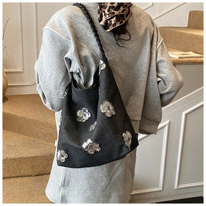 Close-up of black tote bag with silver sequin flowers and a woven shoulder strap