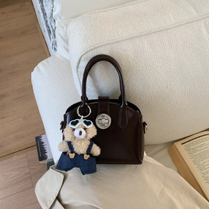 Detail of dark brown leather handbag with silver twist lock and cute teddy bear charm