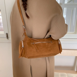 Detail of a brown suede cylinder bag featuring long fringe tassels and a shoulder strap