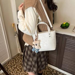 Detailed shot of a white bucket bag with a plush bear charm and detachable strap