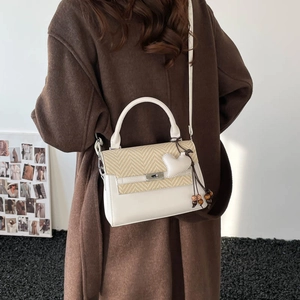 Detail of white leather crossbody bag with beige herringbone weave and heart charm