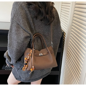 Detail of a dark brown pebble leather crossbody bag with silver lock and boho bead charm