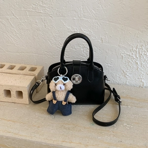 Detail of black matte leather handbag with silver twist lock and cute plush bear charm