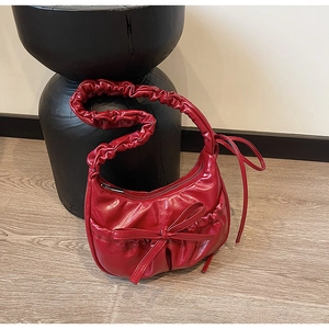 Détail du sac baguette en cuir verni rouge avec décoration nœud et texture plissée