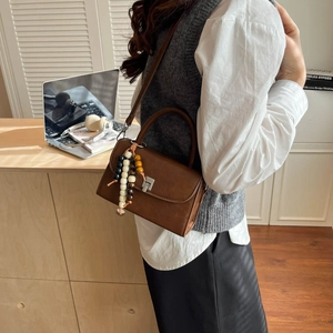 Close-up of a brown matte leather handbag with vintage silver buckle and colorful beaded tassel