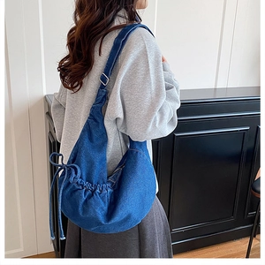Rear view of model wearing a large denim crescent crossbody bag with drawstring detail