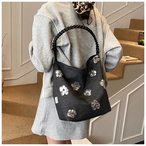 Close-up of a charcoal grey hobo bag with sequin flower patches and woven strap