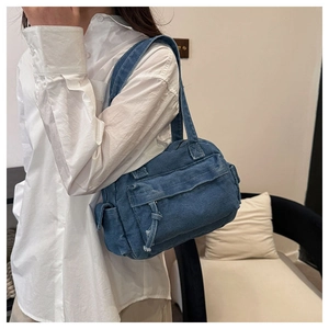 Detailed close-up of blue denim shoulder bag with white stitching and side pockets
