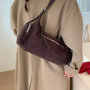 Detailed side view of a dark brown suede cylinder shoulder bag with silver zip and tassels