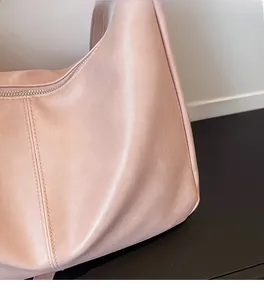 Detail showing soft pink leather texture and fine stitching on a minimalist crossbody bag