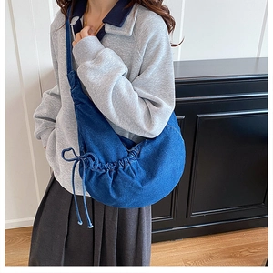 Close-up of a crescent denim crossbody bag with drawstring pleated details on a model