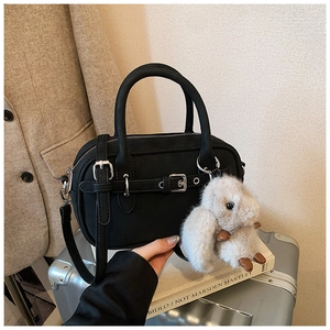 Detail of black leather handbag with decorative straps and a plush brown bunny charm