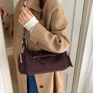 Detail of dark brown suede cylinder bag featuring silver zippers and leather pullers