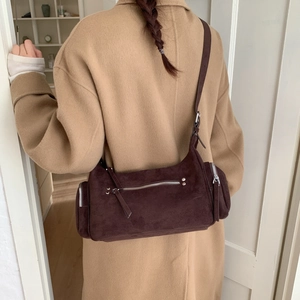 Detail of dark brown suede shoulder bag with zipper pockets worn on a beige coat