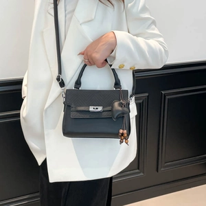 Close-up of black crossbody bag with V-shaped quilting and heart charm on a white blazer