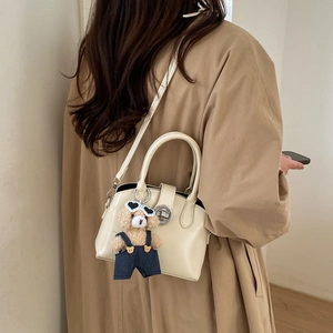 Detail of cream-colored PU leather handbag with gold clasp and plush bear charm accent