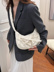 Sac à bandoulière plissé crème à nœud papillon porté par un mannequin dans un cadre minimaliste
