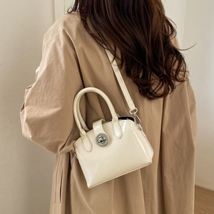 Detail of cream glossy patent leather handbag with silver metal twist lock on a beige coat