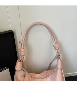 Detail of pink shoulder bag featuring a decorative knotted strap and smooth zipper closure