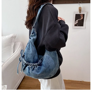 Blue denim hobo bag shown on a model, featuring side drawstring and bow details