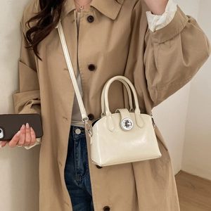 Detail of a minimalist cream white retro handbag with silver clasp on a khaki trench coat
