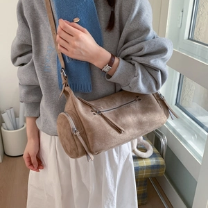 Close-up of brown suede cylinder bag featuring silver zippers and long tassel details