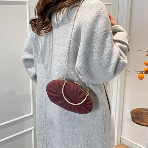 Detail view of burgundy pleated evening clutch with gold chain and metal handle on a model