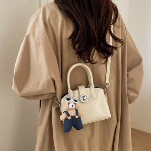 Detail view of cream Boston bag featuring silver twist lock and cute teddy bear charm