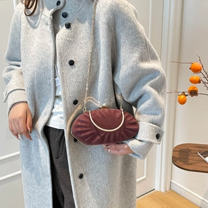 Detail of burgundy satin pleated evening bag with gold chain strap on grey coat