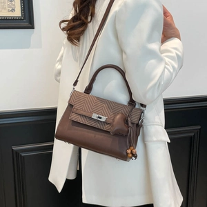 Detail of a brown crossbody bag with herringbone flap and heart pendant on a white suit