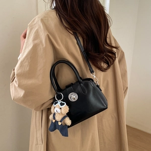 Detail of black faux leather handbag with silver round lock and plush bear pendant