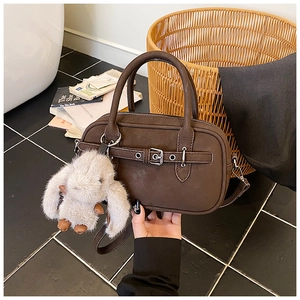 Detail view of dark brown crossbody bag with silver buckles and a plush bunny charm