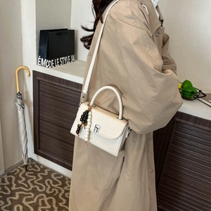 Detail of cream white leather crossbody bag with wooden beads and metal buckle closure