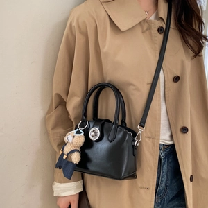 Detail of a black leather handbag featuring a metal twist lock and a cute plush bear charm