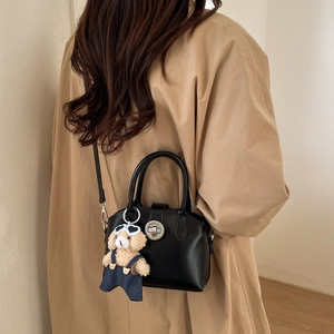 Detail view of black vintage handbag with a cute teddy bear charm on soft beige backdrop