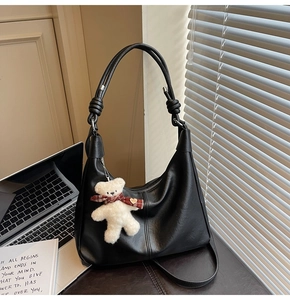 Detail of black pebble PU leather hobo bag featuring knotted shoulder strap and bear charm