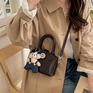 Detail of dark brown leather handbag with teddy bear charm and metal twist lock