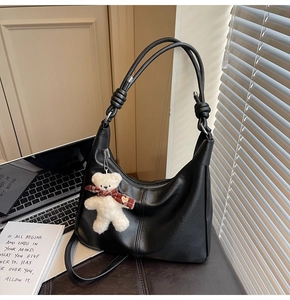 Detail of black leather hobo bag featuring a cute white plush bear charm and knotted straps