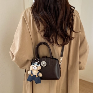 Detail of dark brown leather handbag featuring a silver twist lock and cute bear plush charm