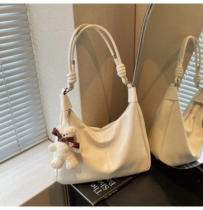 Close-up of cream hobo bag with knotted strap and cute teddy bear plush charm
