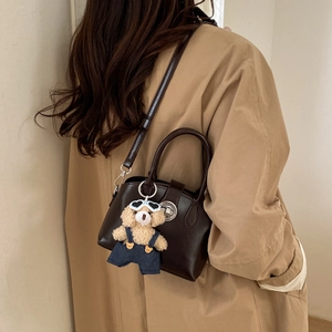 Detailed side view of deep brown retro leather handbag with a cute plush bear charm
